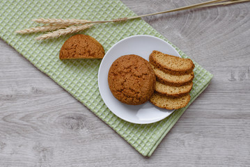 Homemade cookies on a white saucer and green napkins, spikelets of wheat on a wooden background