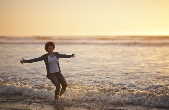 Portrait of a laughing mid adult woman standing ankle deep in the sea at the beach.