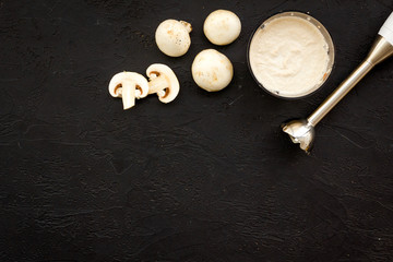 Cook cream soup with mushrooms. Champignon and blender on black background top view copy space