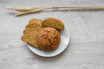 Homemade cookies on a white saucer and spikelets of wheat on a wooden background