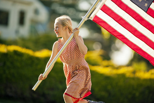 Girl carrying American flag while running through her backyard