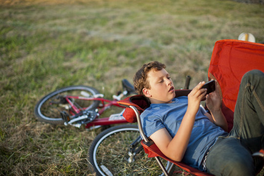 Teenage boy lying in a field looking at a smart phone.