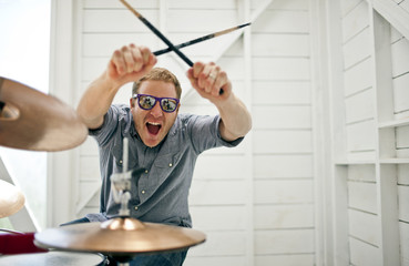 Excited mid adult man gesturing with drumsticks while sitting at a drum kit inside a garage.
