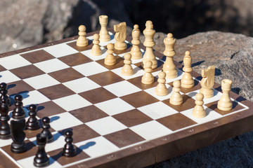 Part of chess board with chess pieces on stone with rock on the background