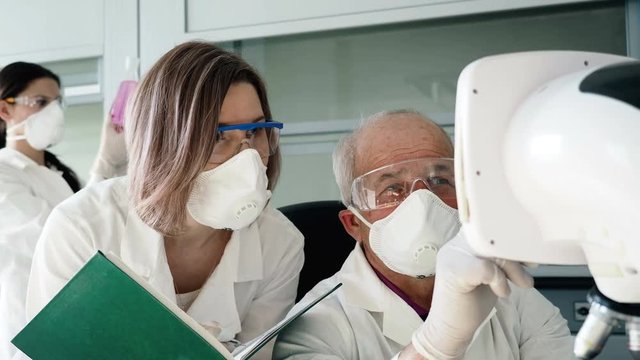 The clinical expertise of dna closeup. Male person checking the material, female assistant write results of analisis to notebook in light cabinet of laboratory. Interns on the scientific genetic exam