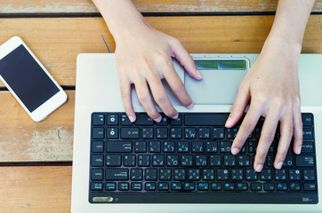 attractive hand of business woman using laptop working typing key board at outdoor on wooden table with mobile phone.