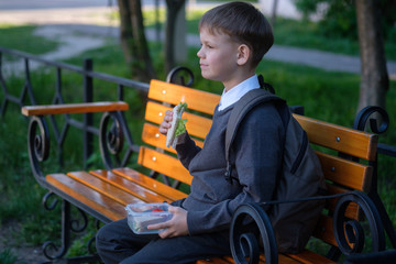 European boy eats school Breakfast on the Park bench