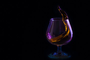 Fototapeta na wymiar splash in a glass of brandy in colored lighting on a black background
