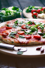 Italian food, cuisine. Margherita pizza on a black, wooden table with igredients like tomatoes, salad, cheese, mozzarella, basil. Delicious homemade food. 
