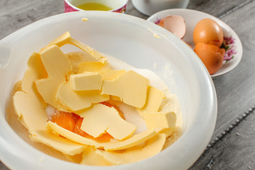 Fototapeta na wymiar White plastic bowl with butter, egg yolks and sugar mixed - preparation for baking a cake.