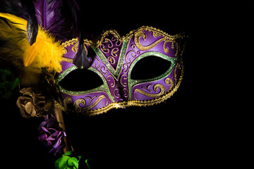 A purple mardi gras or venitian mask with feathers and flowers on a black background with copy space