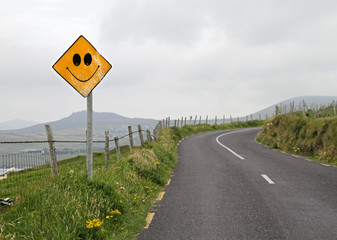 Optimism in cloudy times: Yellow road sign with smiley ahead of curve