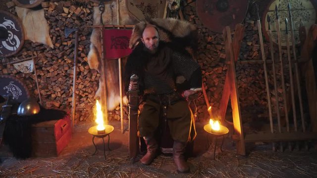 Portrait of a Viking warrior seated on a throne with a sword in his hands.