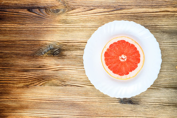 A fresh grapefruit on a white plate on a wooden background