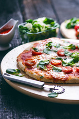 Italian food, cuisine. Margherita pizza on a black, wooden table with igredients like tomatoes, salad, cheese, mozzarella, basil. Delicious homemade food. 