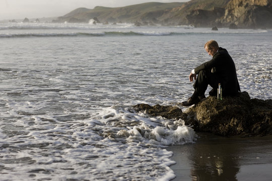 Businessman sitting on rock at beach