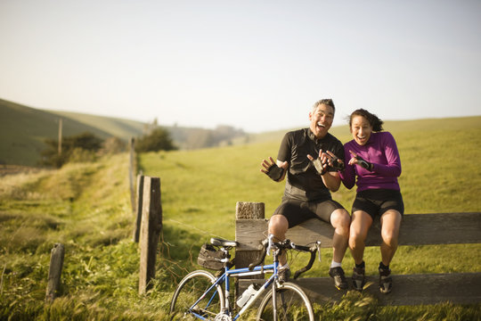 Male and female cyclists sitting on a fence waving their hands and laughing