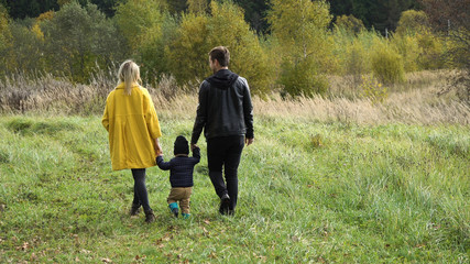 Young family walking in the autumn park with his son, holding his hand.Happy mother, father and little girl walking in autumn park and having fun. Happy young family spending time together outside in