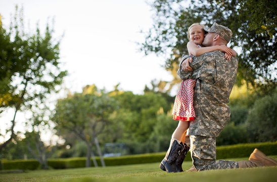 Male soldier hugging his young daughter in the back yard of their home.