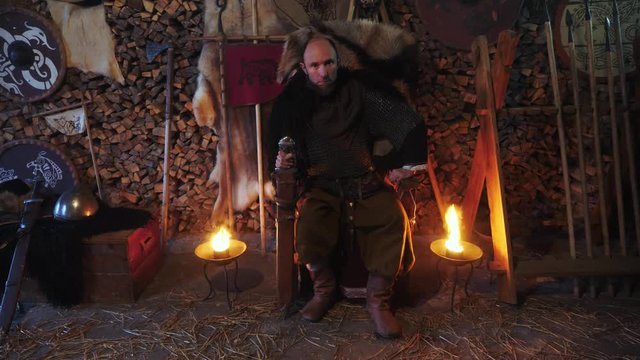 Portrait of a Viking warrior seated on a throne with a sword in his hands.