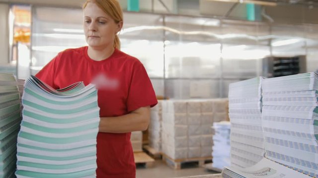 Female worker looking through printed magazines and puts on in stacks in the typography