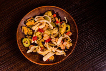 Ceramic plate with different sea food and olives on wooden table. Top view