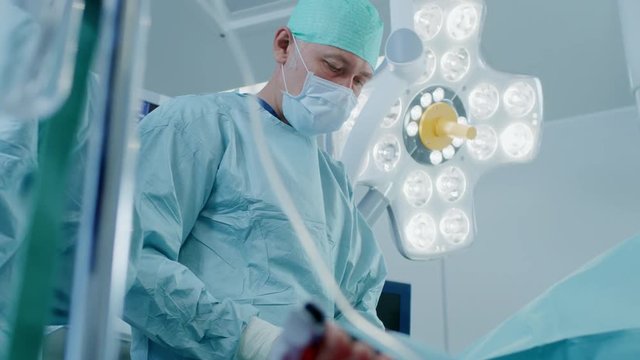 Low Angle Shot in Operating Room, Assistant Passes Instrument to a Chief Surgeon During Invasive Surgery. Professional Doctors Performing Surgery in Modern Hospital.Shot on RED EPIC-W 8K.
