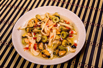 Ceramic plate with different sea food and olives on a bamboo mat