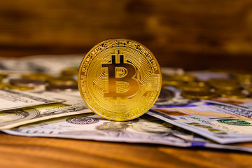 Bitcoins and one hundred dollar bills on wooden table
