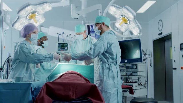Diverse Team of Professional Surgeons Performing Invasive Surgery on a Patient in the Hospital Operating Room. Shot on RED EPIC-W 8K Helium Cinema Camera.