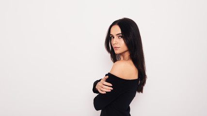Serious woman wearing black dress posing over white wall 