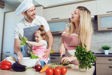 A happy family prepares food from vegetables in the kitchen.
