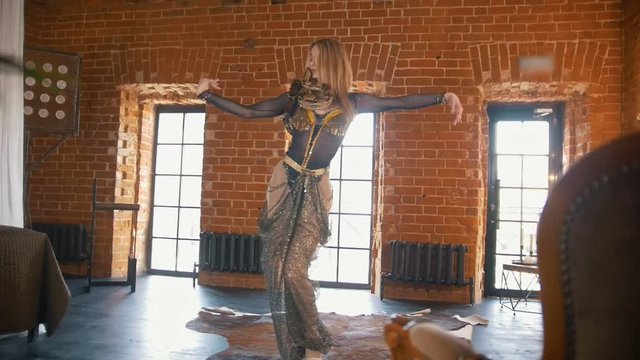 Young woman dances a belly dance in front of a snake in a studio
