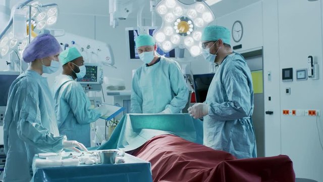 Senior Surgeon Enters Operating Room Where His Assistants and Patient Wait, He Puts on a Mask and Starts Surgery. Real Modern Hospital with Authentic Equipment.