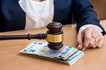 Woman holds wooden hammer over banknotes in euros