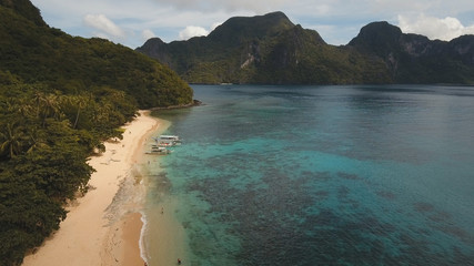 Beautiful beach with boats and tourists. Tropical bay in El Nido. Aerial view: bay and the tropical island. Tropical lagoon with turquoise water and white sand. Seascape: mountains, ocean. Sky and
