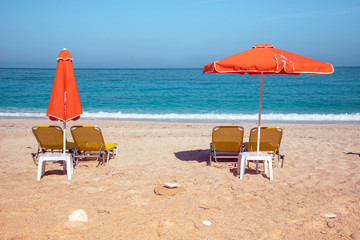 Abstract image with sun loungers and orange umbrellas from the sun on the beach on the seafront with waves (relaxation, harmony, holidays - concept)