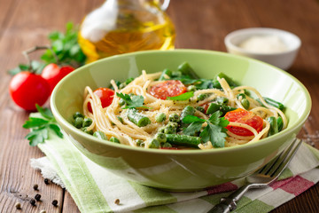 Spaghetti pasta with green beans, peas, cherry tomatoes, parsley and parmesan cheese on wooden table