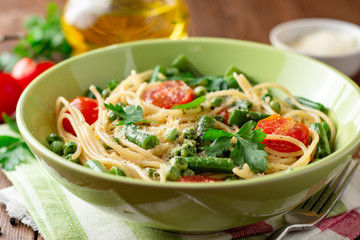 Spaghetti pasta with green beans, peas, cherry tomatoes, parsley and parmesan cheese on wooden table