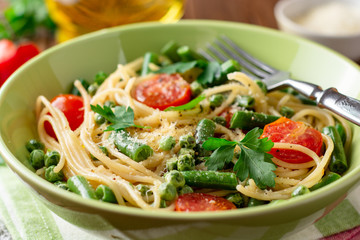 Spaghetti pasta with green beans, peas, cherry tomatoes, parsley and parmesan cheese on wooden table