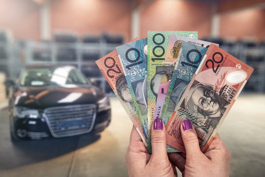 Australian dollar in hands on background of new cars