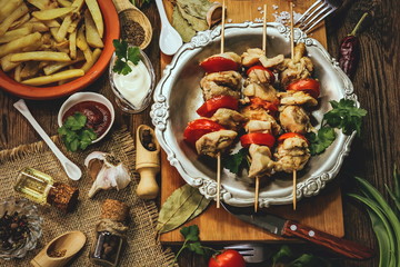 fried chicken meat with tomatoes on wooden sticks. Barbecue with vegetables on a wooden background.