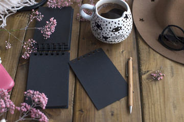 A cup of fragrant coffee and a black notepad for notes. Good morning . Women's accessories and pink flowers. Light from the window. Place for text. Horizontal photo.