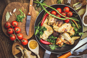 fried chicken wings in a frying pan with tomatoes. wooden background
