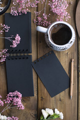 A cup of fragrant coffee and a black notepad for notes. Good morning . Wooden background. Light from the window. Place for text. Vertical photo.