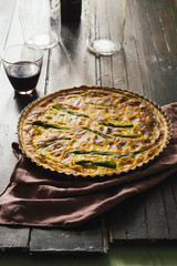 Quiche with green asparagus
, egg, cream, scamorza cheese and spec ham, round shaped on an aluminium mold, frontal view
over a wooden board with ingredients around.