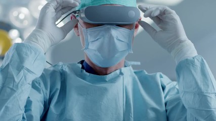 In the Hospital Operating Room Professional Surgeon Puts on Virtual Reality Glasses. Shot on RED EPIC-W 8K Helium Cinema Camera. - Powered by Adobe