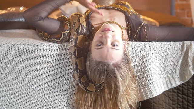 Python crawling on the body of young smiling female dancer on the bed