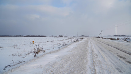 Countryside road through winter field with forest on a horizon. Winter landscape countryside, forest, field.