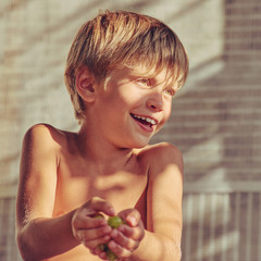 Smiling happy blond boy eating green grapes, image with square aspect ratio and warm toning